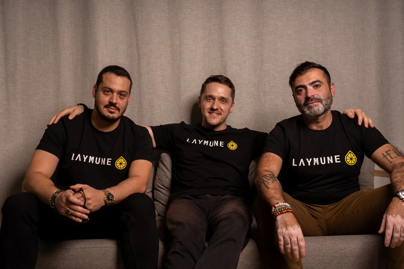 The three Laymune co-founders sitting together on a sofa in matching black T-shirts.